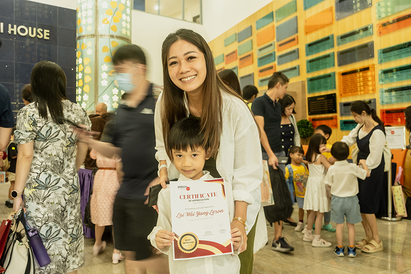 A parent and child proudly holding a Speech Academy Asia certificate at a graduation event